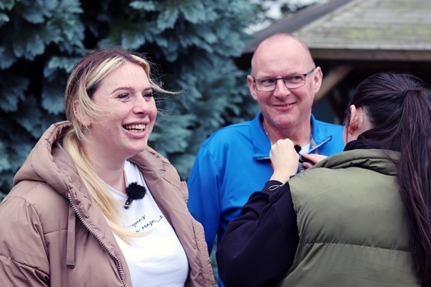The photo shows 2 people, Marileigh and Craig standing side by side , outside in front of some trees.
